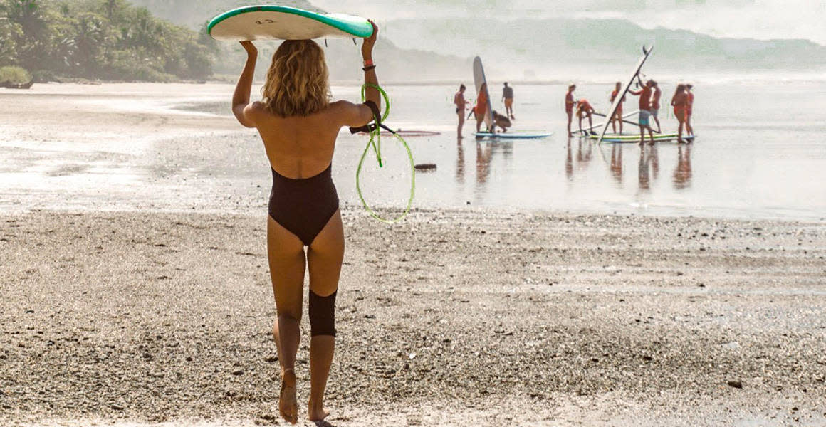 girl with the surfboard on top walking on the beach