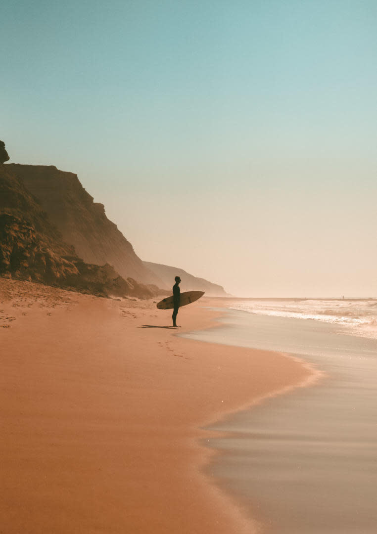 man standing on beach surfboard